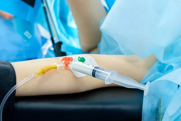 A catheter with a syringe in the hand of a patient lying on an operating table. The process of surgery under general anesthesia. Anesthesia is administered through a syringe. The patient is sleeping.
