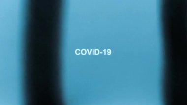Beyaz yazıt COVID-19, röntgen şeklinde. Mavi arka planda siyah çizgiler sağa sola hareket eder. 