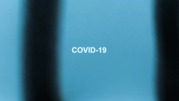 Witte inscriptie COVID-19 in de vorm van een röntgenfoto. Zwarte strepen bewegen van links naar rechts op een blauwe achtergrond. — Stockvideo