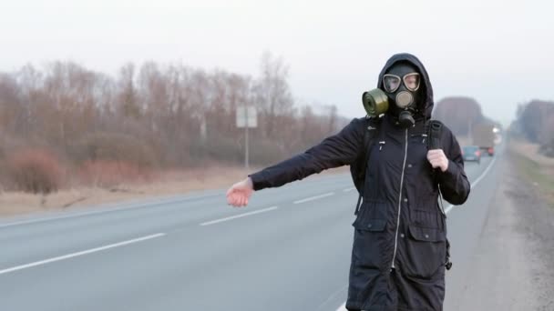 Dívka v plynové masce stojí na kraji silnice a snaží se zastavit auto. — Stock video