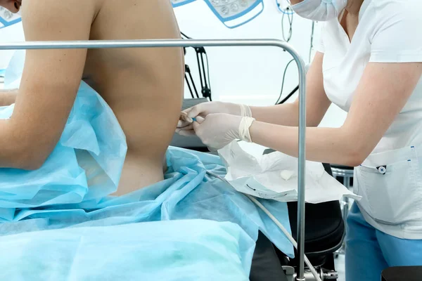 Un anestesista con ropa médica blanca, una máscara y guantes estériles sostiene una aguja en sus manos . —  Fotos de Stock