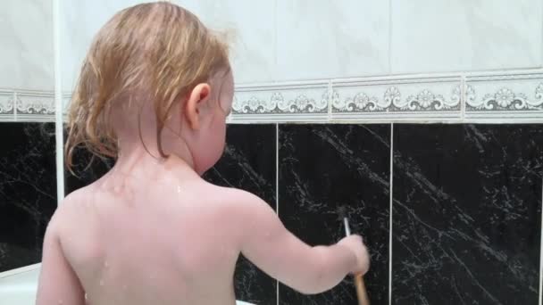 La piccola bionda si bagna in bagno e dipinge con una spazzola sul muro . — Video Stock