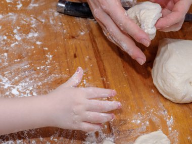 Anne ve küçük kızın elleri hamuru ahşap bir masada yoğurur. Aile yemekleri kavramı ebeveynleri ve çocukları bir araya getirir..