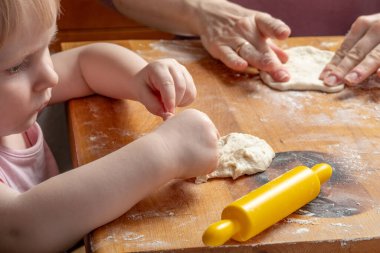 Anne ve küçük kızın elleri hamuru ahşap bir masada yoğurur. Aile yemekleri kavramı ebeveynleri ve çocukları bir araya getirir..