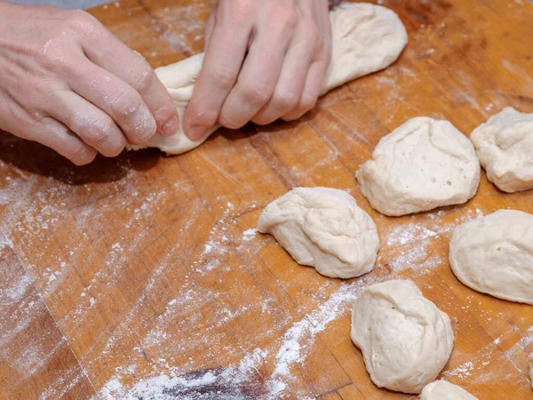 Female hands knead the dough on a wooden table. The process of preparing fresh elastic baking dough. Table and hands in flour. Natural home cooking.