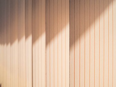 Pencereyi kaplayan dikey panjurların tekstil lamellaları. Güneş ışığının donuk ışınları soyut bir model oluşturur. Sıcak, huzurlu bir atmosfer..