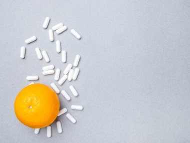 Beyaz büyük oval haplar ve gri arka planda olgun turuncu. Sentetik ya da doğal vitaminler. İlaçları ve doğal meyveleri seçme kavramı. Boşluğu kopyala.