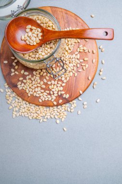 Yerleşim planı. Gri arka planda tahta bir standın üzerinde duran Sibirya sedir cevizli cam kavanoz. Yakınlarda bir tahta kaşık var. Fındıklar yüzeye saçılmış. Vitamin ve mineral açısından zengin yiyecekler. Boşluğu kopyala