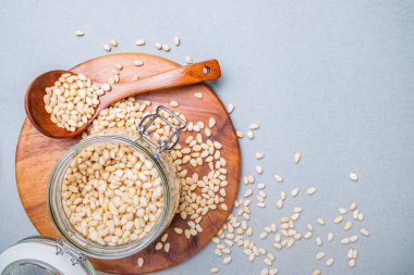 Yerleşim planı. Gri arka planda tahta bir standın üzerinde duran Sibirya sedir cevizli cam kavanoz. Yakınlarda bir tahta kaşık var. Fındıklar yüzeye saçılmış. Vitamin ve mineral açısından zengin yiyecekler. Boşluğu kopyala