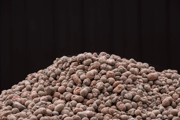A mountain of clay expanded clay granules on a dark brown background. Expanded clay as a building material and as a drainage for plants. — Stock Image Mountain Clay Expanded Clay Granules Dark Brown Background Expanded Clay Royalty Free Stock Photos