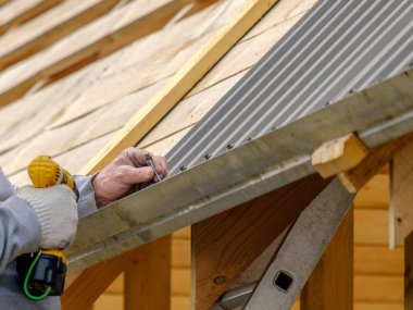 Sarı bir tornavidayla çalışan erkeklerin elleri çatı katını bir kır evinin çatısına vidalayabilir. Kablosuz matkap. Elektrik mühendisliği ve teknoloji kullanımı.