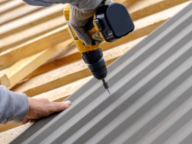 Sarı bir tornavidayla çalışan erkeklerin elleri çatı katını bir kır evinin çatısına vidalayabilir. Kablosuz matkap. Elektrik mühendisliği ve teknoloji kullanımı.