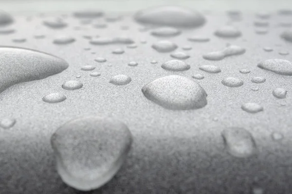 Transparent drops of water on a silver glossy metal surface. Abstract background with strong blur zone of blur.