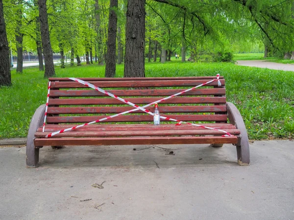 城市公园的长椅被红白相间的警戒线包裹着 长椅上有一瓶空的伏特加 Coronavirus大流行病检疫期间的限制性措施 — 图库照片