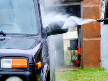 Öğleden sonra yüksek basınçlı bir aletle dışarıda araba yıkama. Suyla dolu güçlü bir sprey arabanın mor vücudundaki kiri, camları, tekerlekleri ve lastikleri temizler..