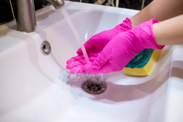 A hand in a pink glove washes a washbasin in the bathroom with a sponge with foaming detergent. Cleaning company cleans the house. Disinfection of the senile node from viruses and bacteria.