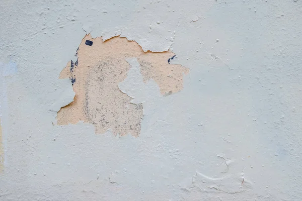 Light gray paint peels off the surface of an old metal sheet. On the bottom layer peach-colored paint is exposed. Grunge pattern.