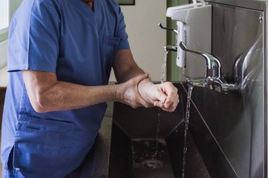Doktor ellerini paslanmaz çelik bir lavaboda musluğun altında yıkıyor. Dezenfeksiyon ve sterilizasyon. Bakteri ve virüsleri temizliyorum. Gerekli dezenfeksiyon önlemleri. Su sıçrıyor..