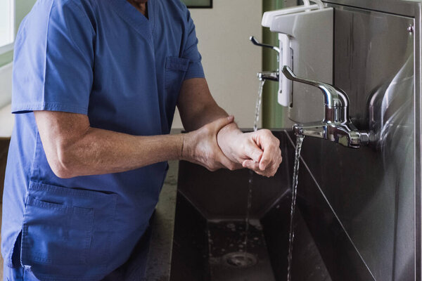 The doctor washes his hands under the tap in a stainless steel sink. Disinfection and sterilization. Removing bacteria and viruses. Necessary disinfection measures. Splashing water.