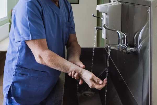 The doctor washes his hands under the tap in a stainless steel sink. Disinfection and sterilization. Removing bacteria and viruses. Necessary disinfection measures. Splashing water.