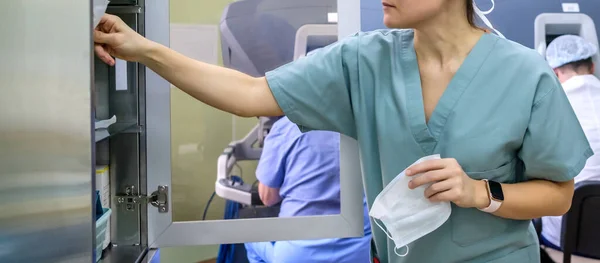 一名女医生手里拿着医疗面罩 从橱柜里拿出医疗用品 穿着绿色制服的医生 背景是医生和现代医疗设备 — 图库照片