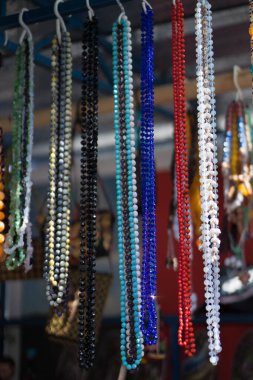 Farklı taşlardan boncuklar bir stantta asılı.