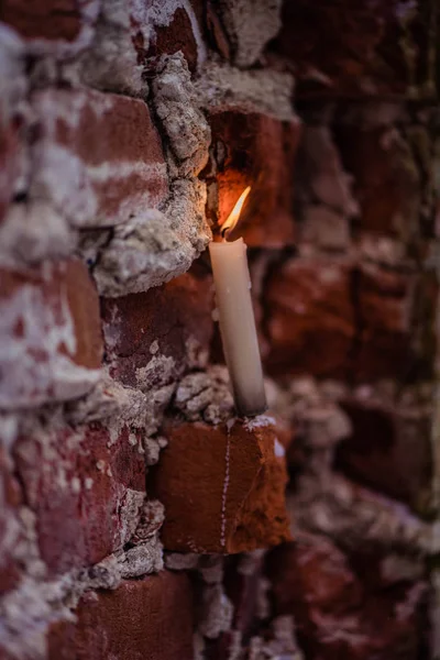 Vela de cera branca queima em um fundo de tijolo — Fotografia de Stock