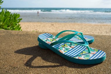 Denizin arkasındaki kumsal için mavi parmak arası terlikler.