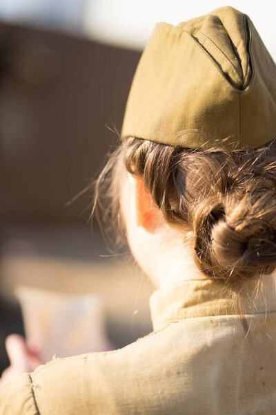 girl in uniform stands with her back on a big scythe