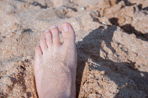 Children's foot in the sand on the beach. White sand