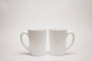 Beyaz bir kupa beyaz bir arkaplanda bir masanın üzerinde duruyor..