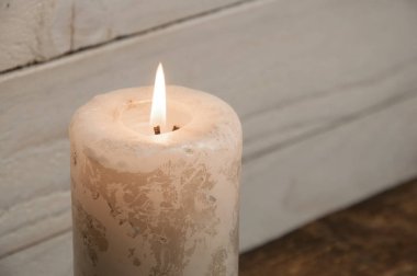 Ahşap bir masada duran büyük bir mum yanar. Noel