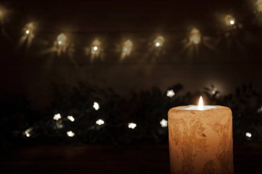 Siyah arka planda büyük bir mum karanlıkta yanar. Çelenk ışıkları ve yıldızlar. Noel ve Yeni Yıl