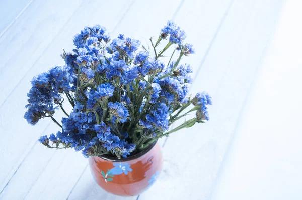 Vase with little blue flowers. On white background. Still life