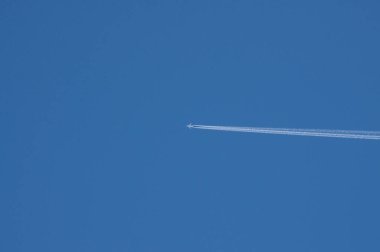 Beyaz bir uçak uçar ve ardında dumandan bir iz bırakır. Mavi gökyüzüne karşı