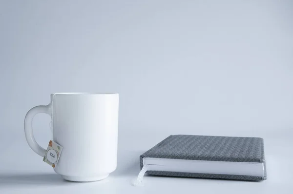 White cup and closed book or notepad. On white background.