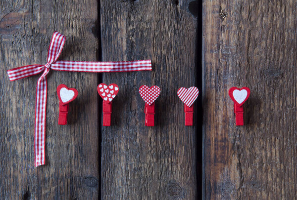 Little red clothespins hearts and bow on a wooden background. Love