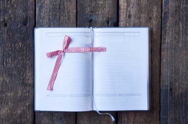 Boş beyaz sayfalı defteri aç. Sevimli kırmızı fiyonk. Ahşap bir arka planda.