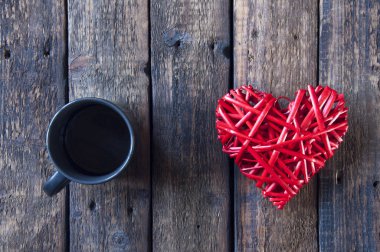 Sevgililer günü için kırmızı hasır bir kalp ve ahşap bir masada çay ya da kahve olan siyah bir bardak. Yukarıdan görüntüle.