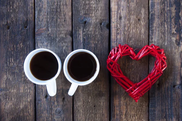 Red wicker heart and two white cups with tea or coffee. On a wooden table