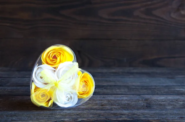 White and yellow rose flowers are packed as a gift. On a wooden background.
