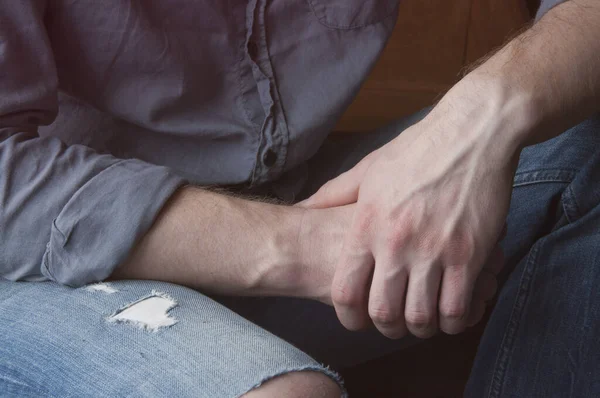 Hands of a man. Clasped hands. In a shirt and jeans.