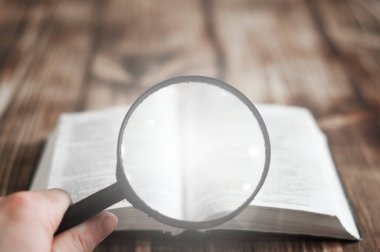 Tahta bir masanın üzerinde açık İncil. Büyüteç