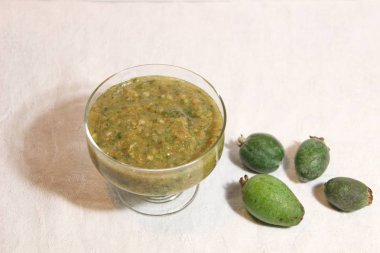 Beyaz arka planda cam kasede yeşil feijoa reçeli