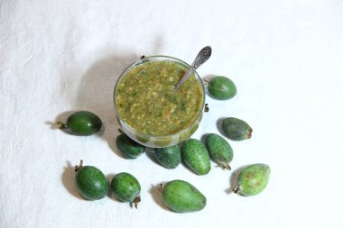 Yeşil Fayjoa, cam kasede şekerle bembeyaz arka planda kaşıkla öğütülmüş.