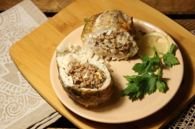 Karabuğdayla doldurulmuş fırında balık, limon dilimi, ahşap arka planda kırsal kapakta maydanoz.