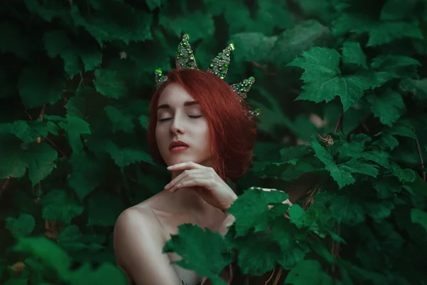 Portrait of a girl with red hair in a green leaves with a crown — Stock Photo, Image