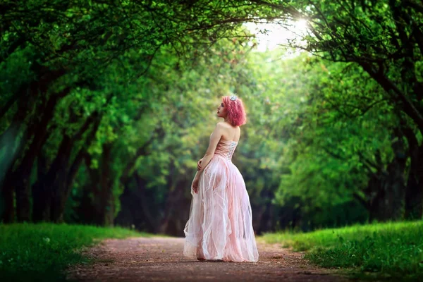 一个漂亮的女孩穿粉红色衣服的肖像。站在人行道上。浪漫的女人，在童话森林里的肖像。童话故事公主步行穿过雾气弥漫的森林. — 图库照片