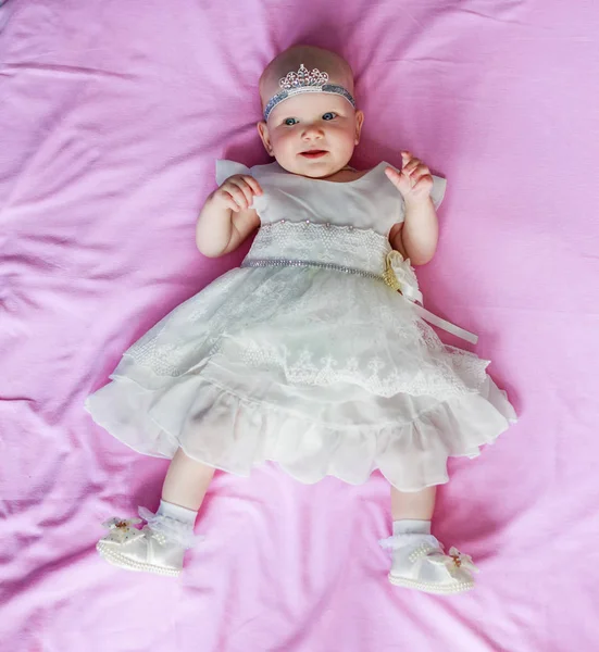 Retrato de uma menina bonita com uma coroa na cabeça deitado fundo rosa — Fotografia de Stock