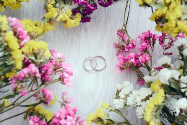 Close-up view of golden wedding rings and beautiful small flowers on wooden tabletop clipart
